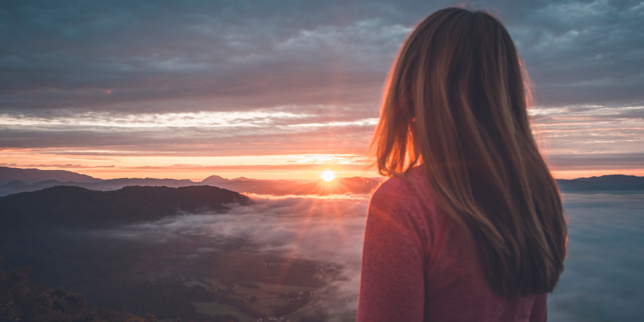 A person staring into the sunset with a view of the mountains and fog.
