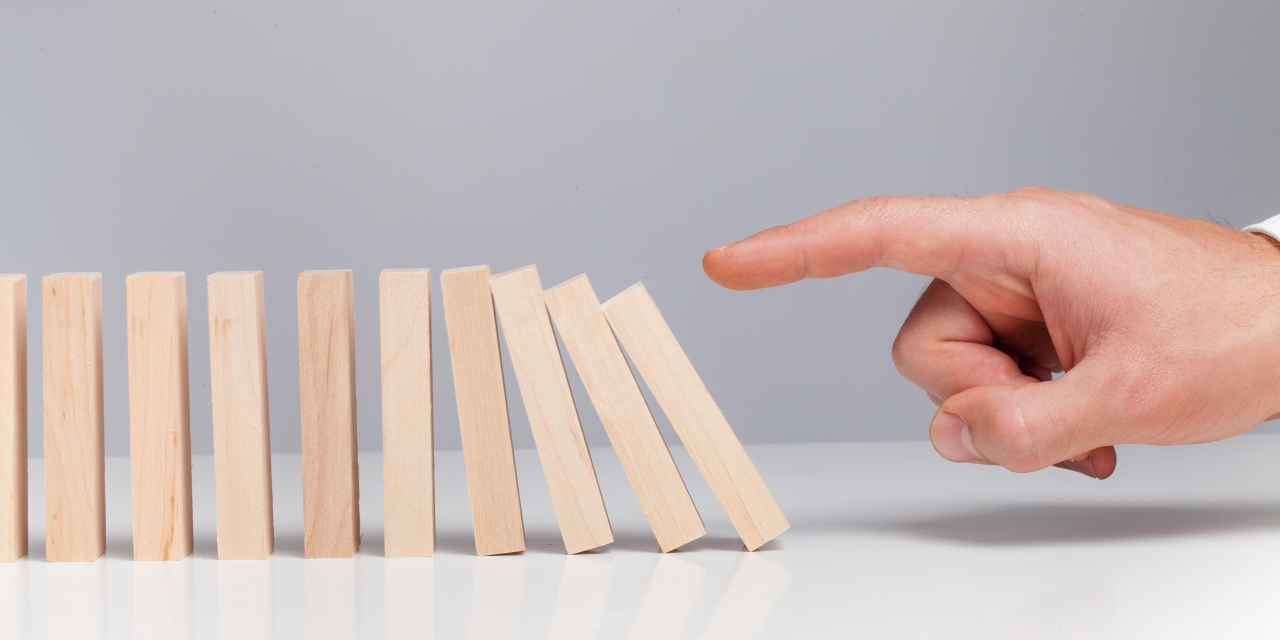 A person's hand pushing down wooden dominoes