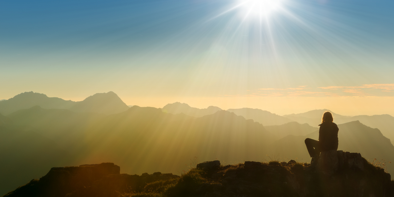 person sitting on mountain summit at dawn